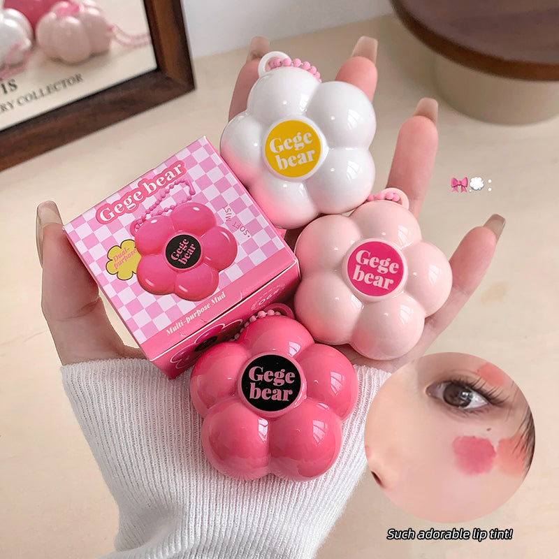 Pink and white 'Gege bear' lip balm with packaging held by a hand, close-up of application on skin.