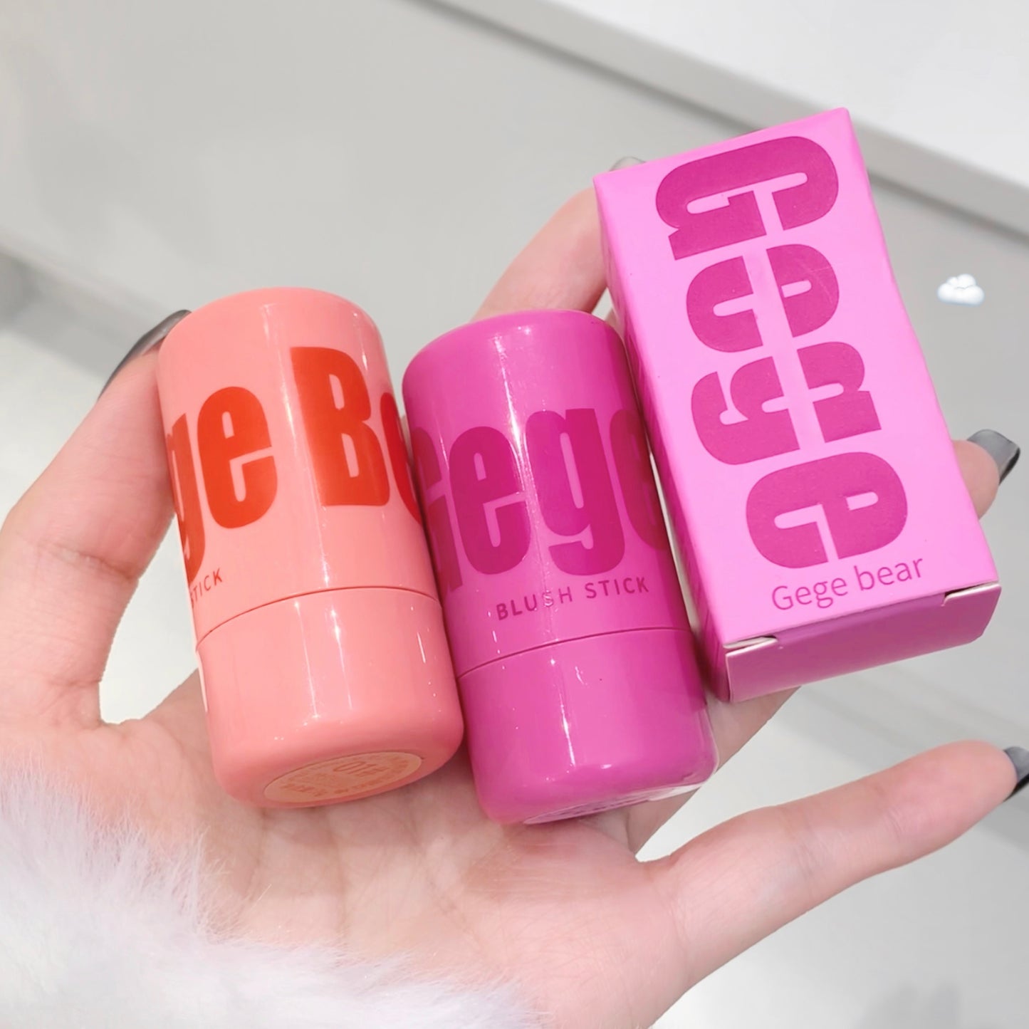 Two blush sticks and their packaging held in a hand with a white background