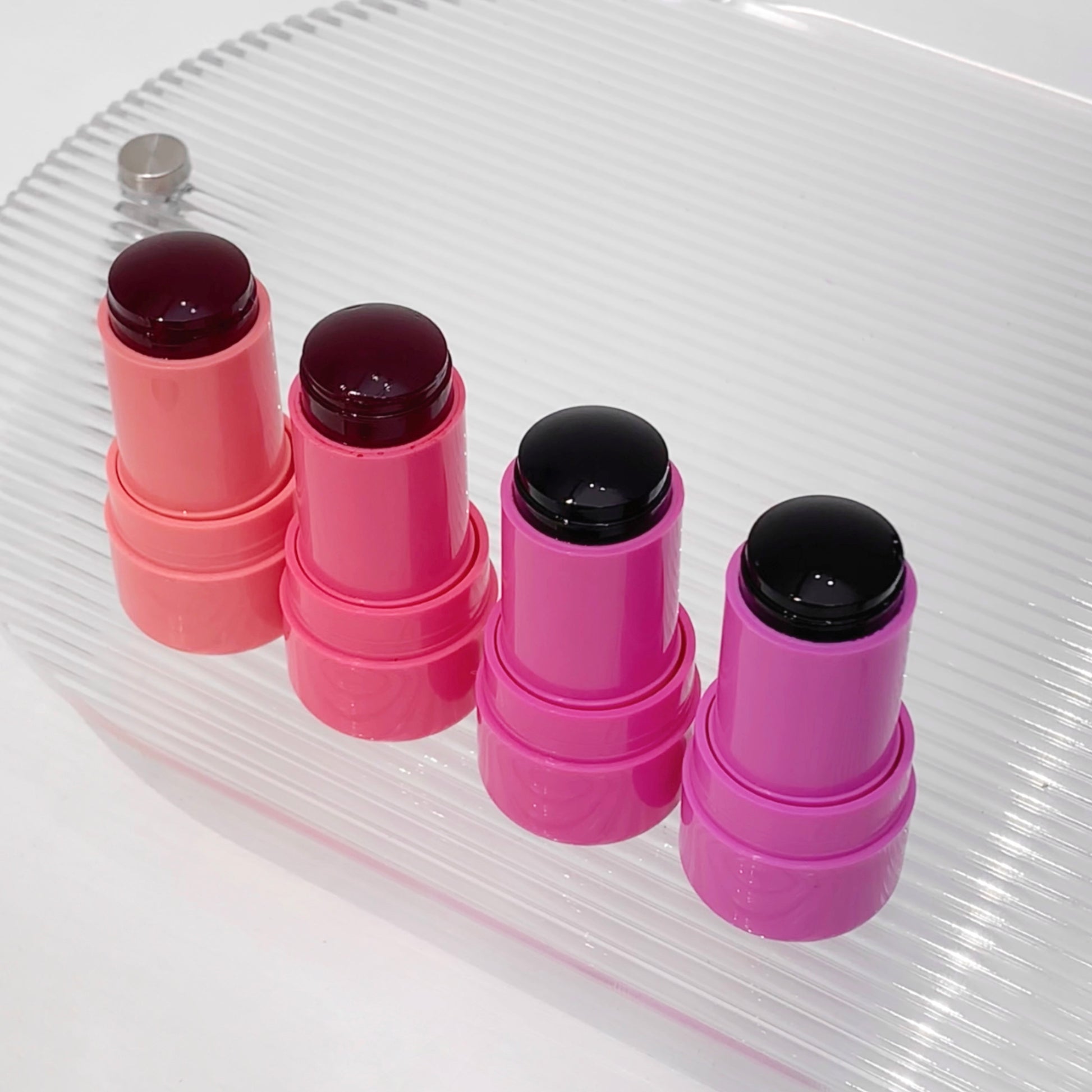 Four pink lip balms with black caps on a clear glass surface