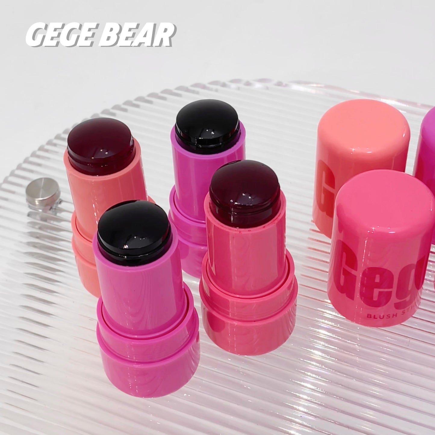 Pink lipsticks with black caps on a clear glass plate, featuring the brand 'GEGE BEAR'.