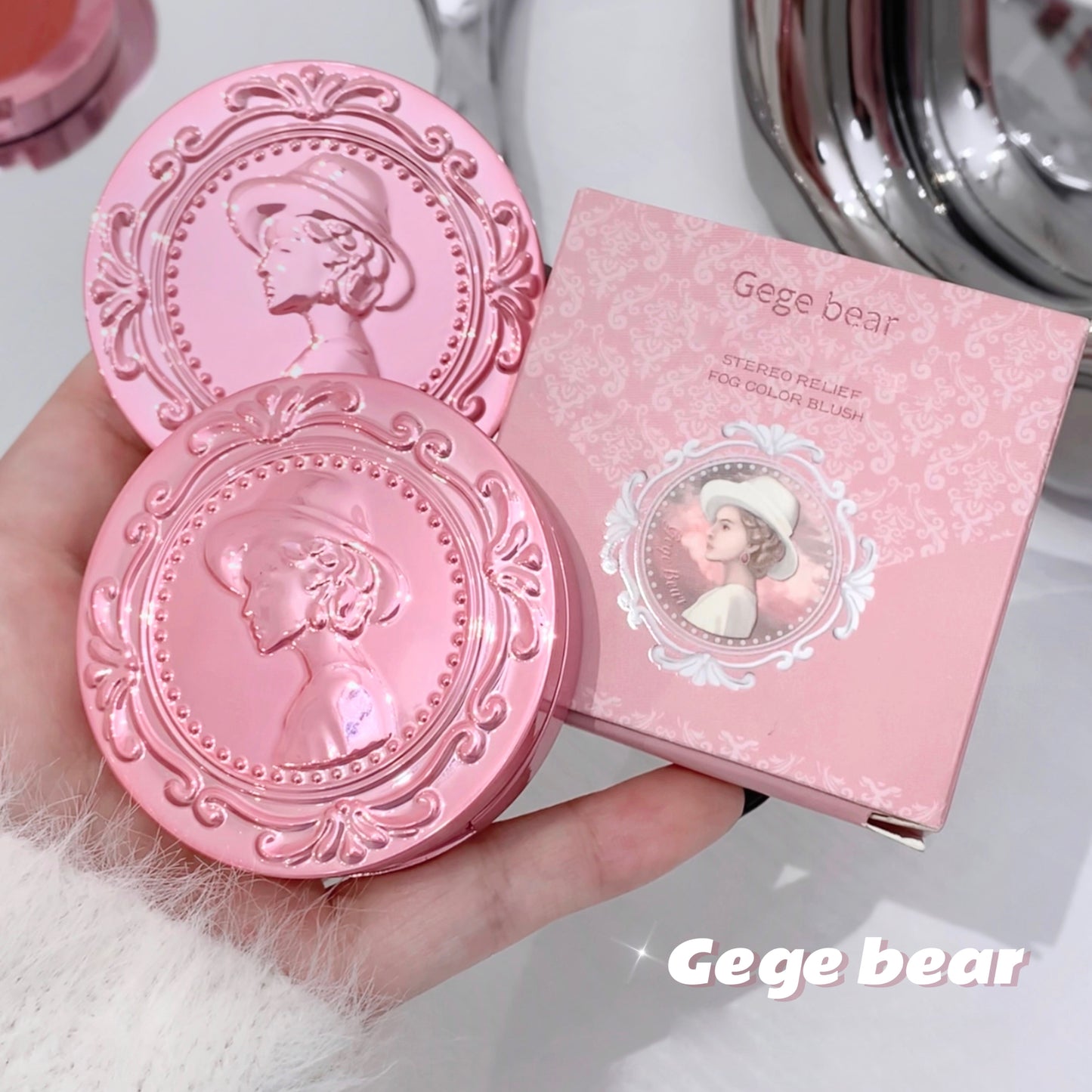 Pink makeup compact with decorative lid and matching box held by a hand, brand 'Gege bear' visible.