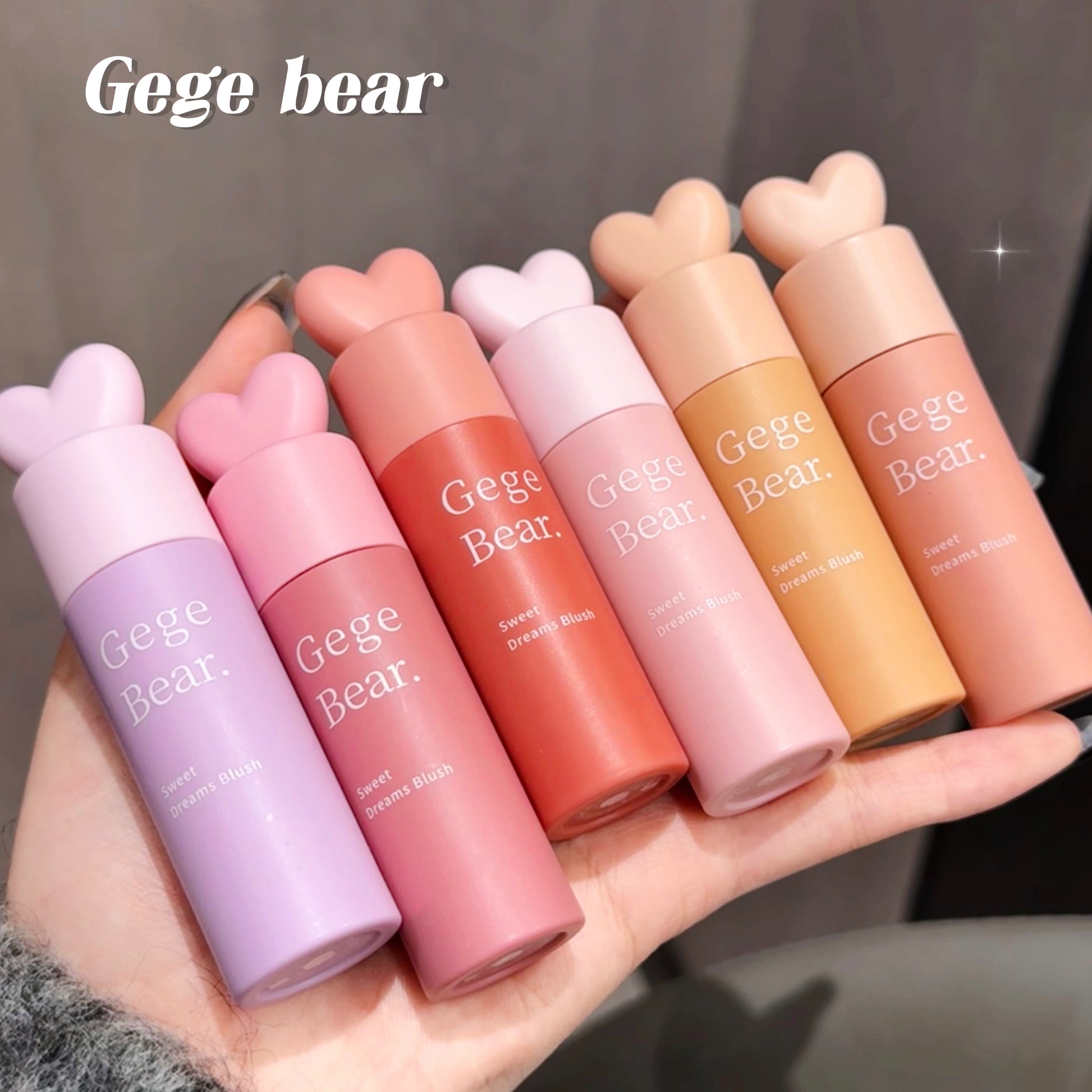 Set of Gege Bear lip glosses held in a hand against a neutral background