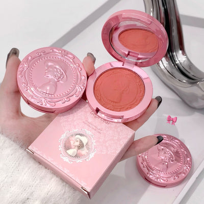 Pink blush compact with decorative lid held by a hand on a white background