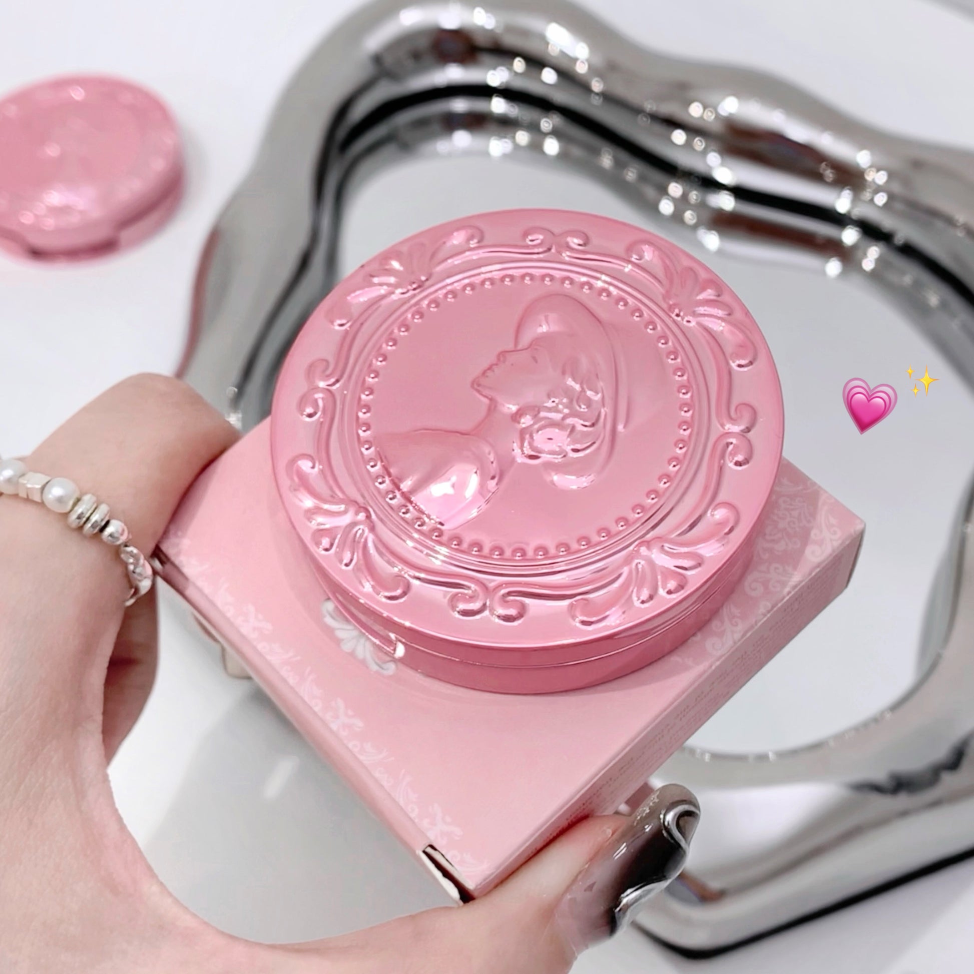 Pink compact mirror with decorative design held by a hand on a white background