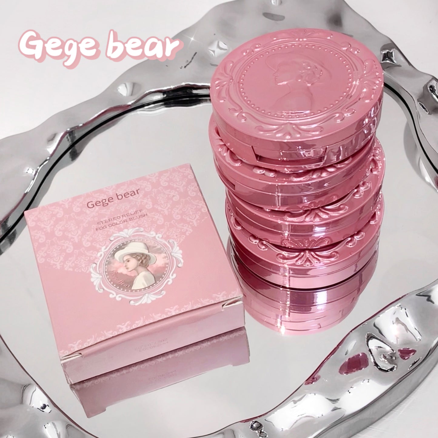Stack of pink compacts and packaging on a silver tray with 'Gege bear' branding.