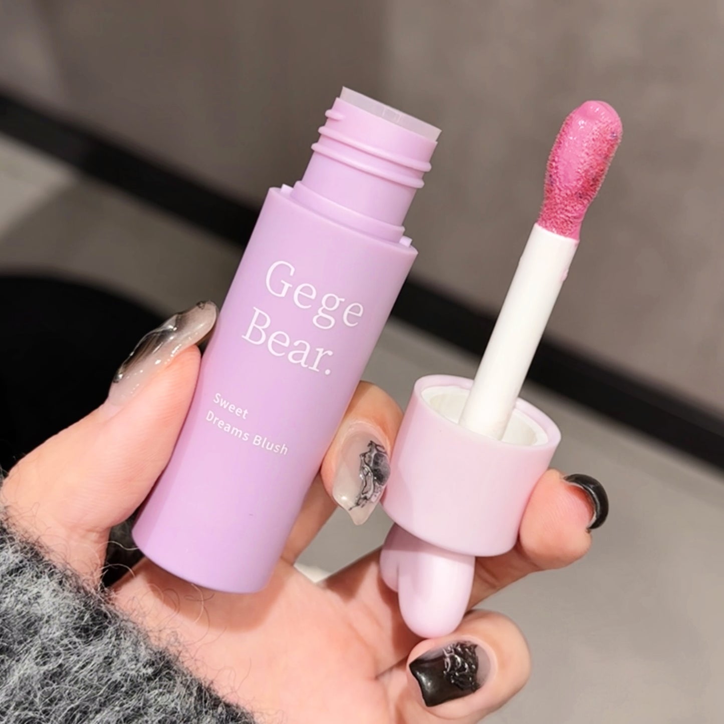 Lip gloss with pink cap and purple body held by a hand, brand 'Gege Bear' visible.