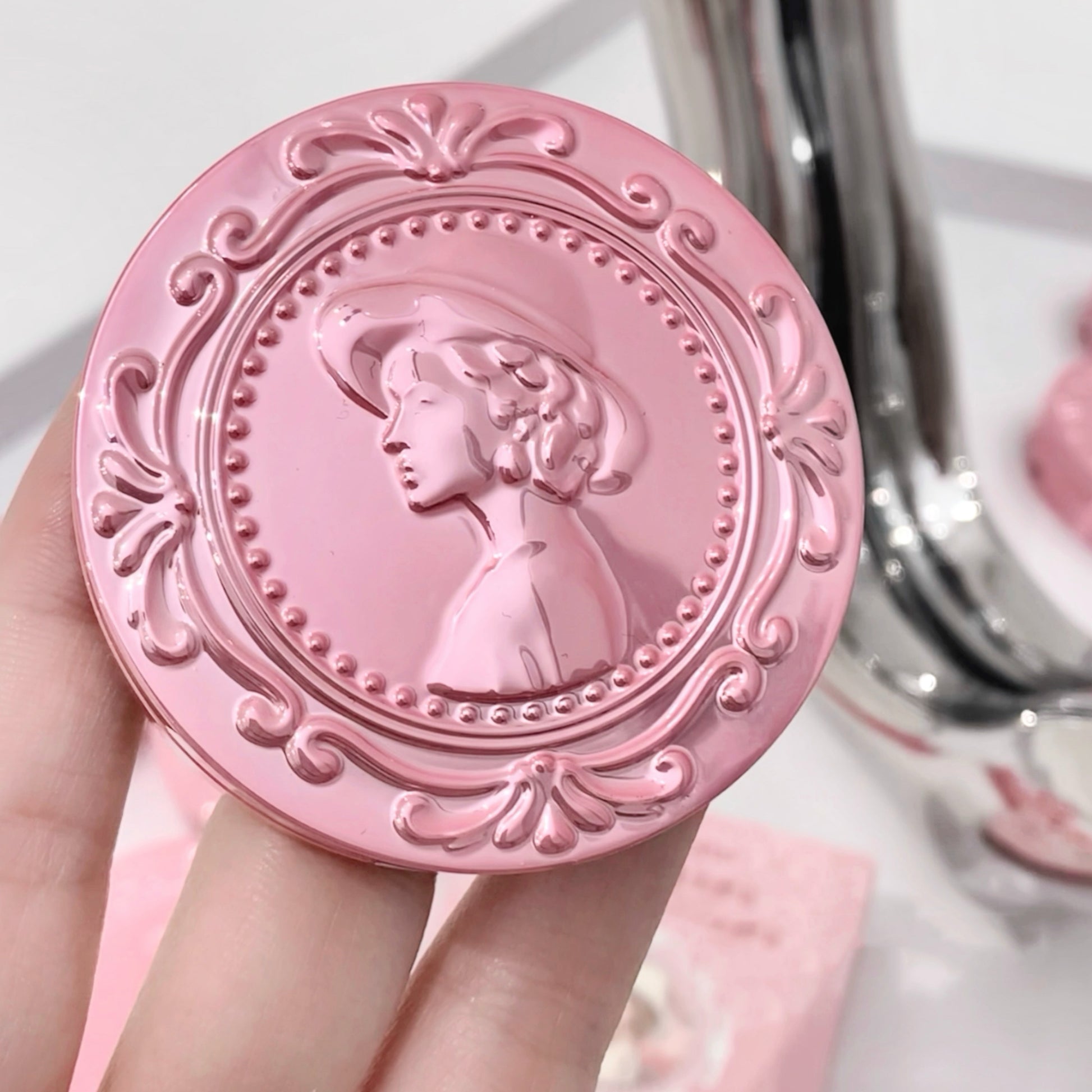 Pink decorative compact mirror with a profile design held by a hand.