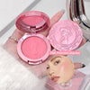 Pink makeup compact with decorative lid held by a hand, showing blush color on a white background.