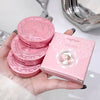 Pink compact mirrors and their packaging held in a hand with a bathroom background.