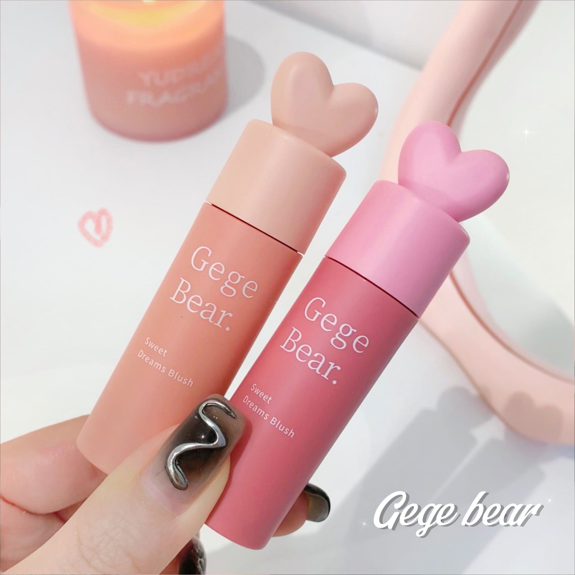 Two pink Gege Bear makeup products held by a hand with a blurred background.