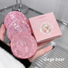 Pink decorative coasters with a matching box held by a hand on a reflective surface.