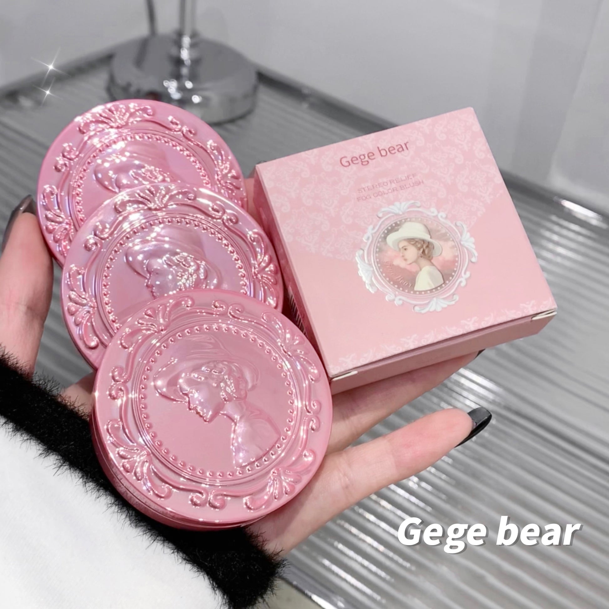Pink decorative coasters with a matching box held by a hand on a reflective surface.