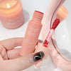 Hand holding a pink makeup product with 'Gege Bear' branding, blurred candle in the background