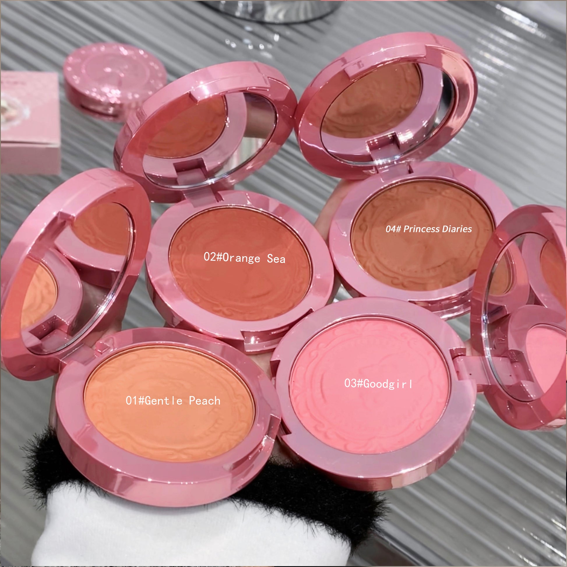 Multiple pink blush compacts with different shades on a reflective surface.