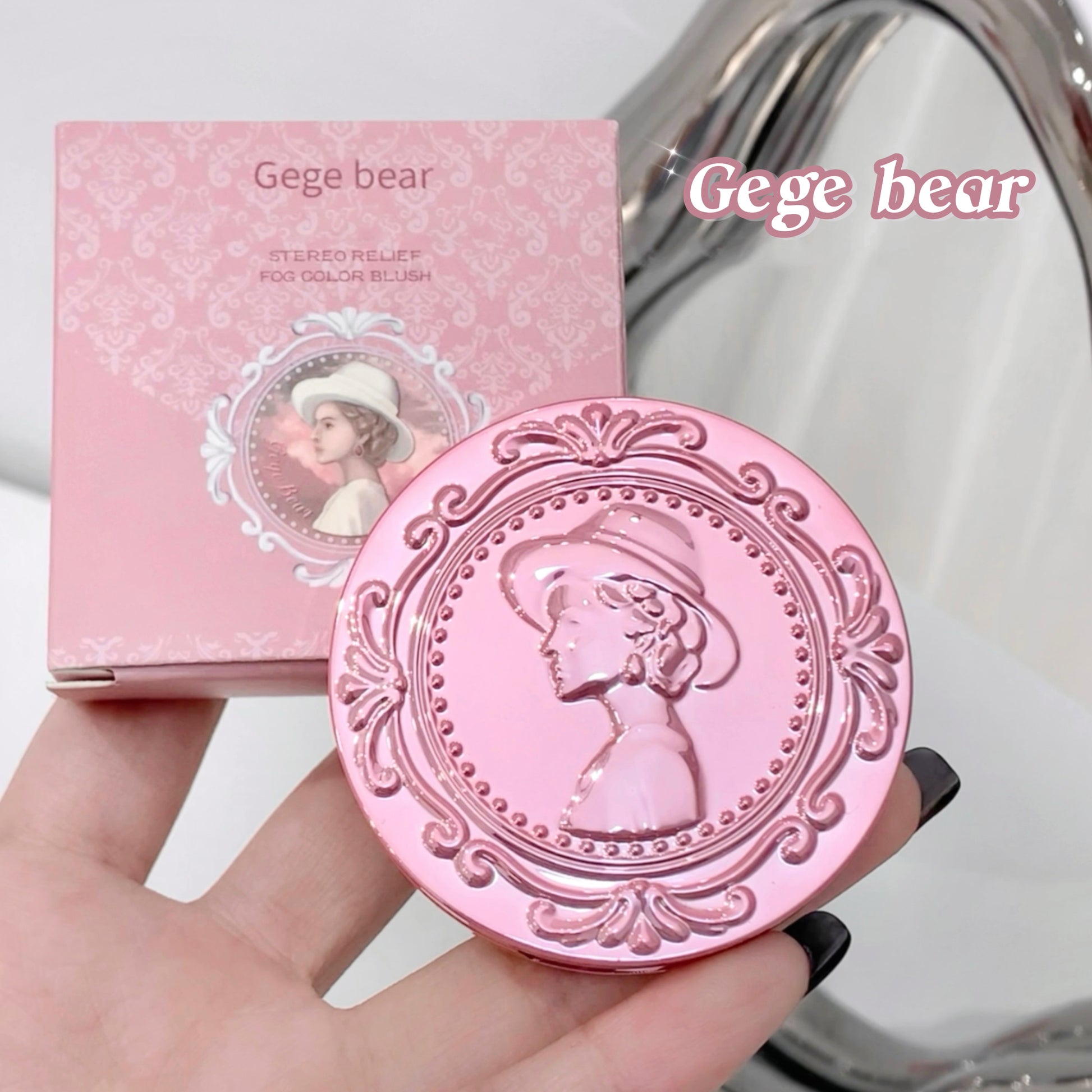 Pink compact mirror with decorative design held by a hand, next to its packaging labeled 'Gege bear'.