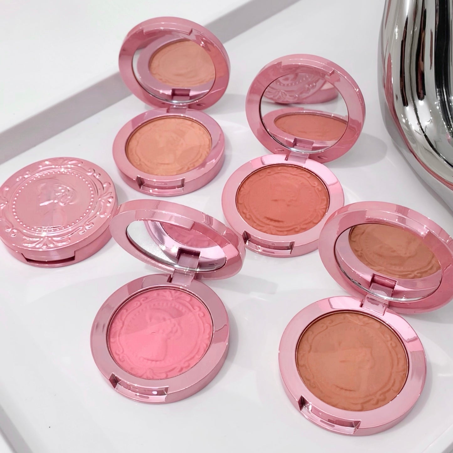 Pink makeup compacts with blushes on a white surface