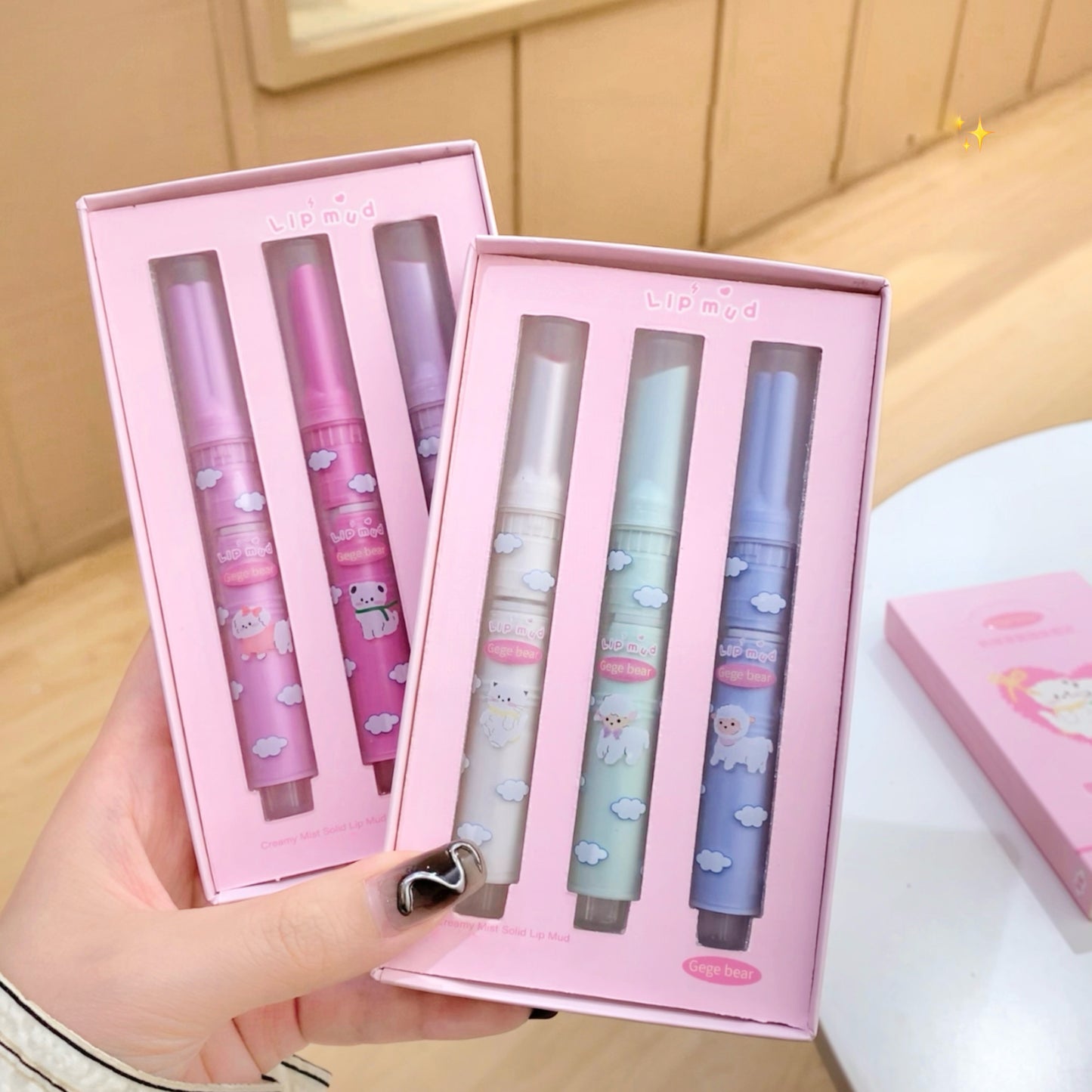Set of four lip balms in pink packaging held by a hand on a light wooden surface.