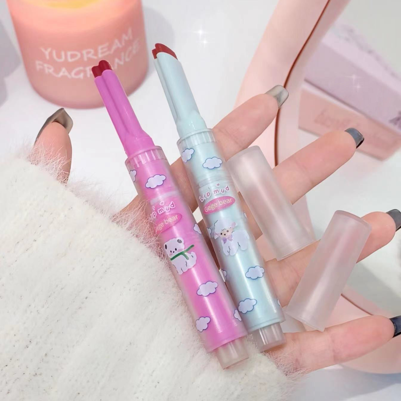 Two colorful lip balms with cartoon designs held by a hand on a light background.