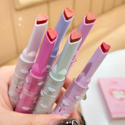 Set of colorful lip-shaped markers with heart caps held in a hand against a neutral background.