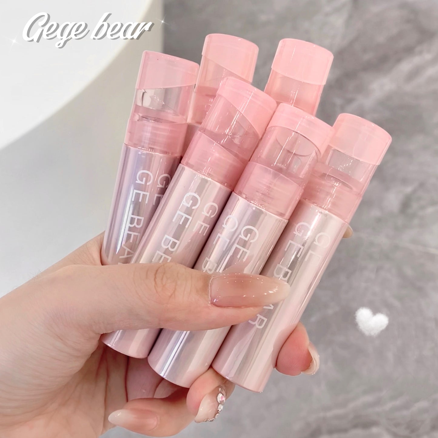 Hand holding pink lip balms with 'Gee Bear' branding against a neutral background