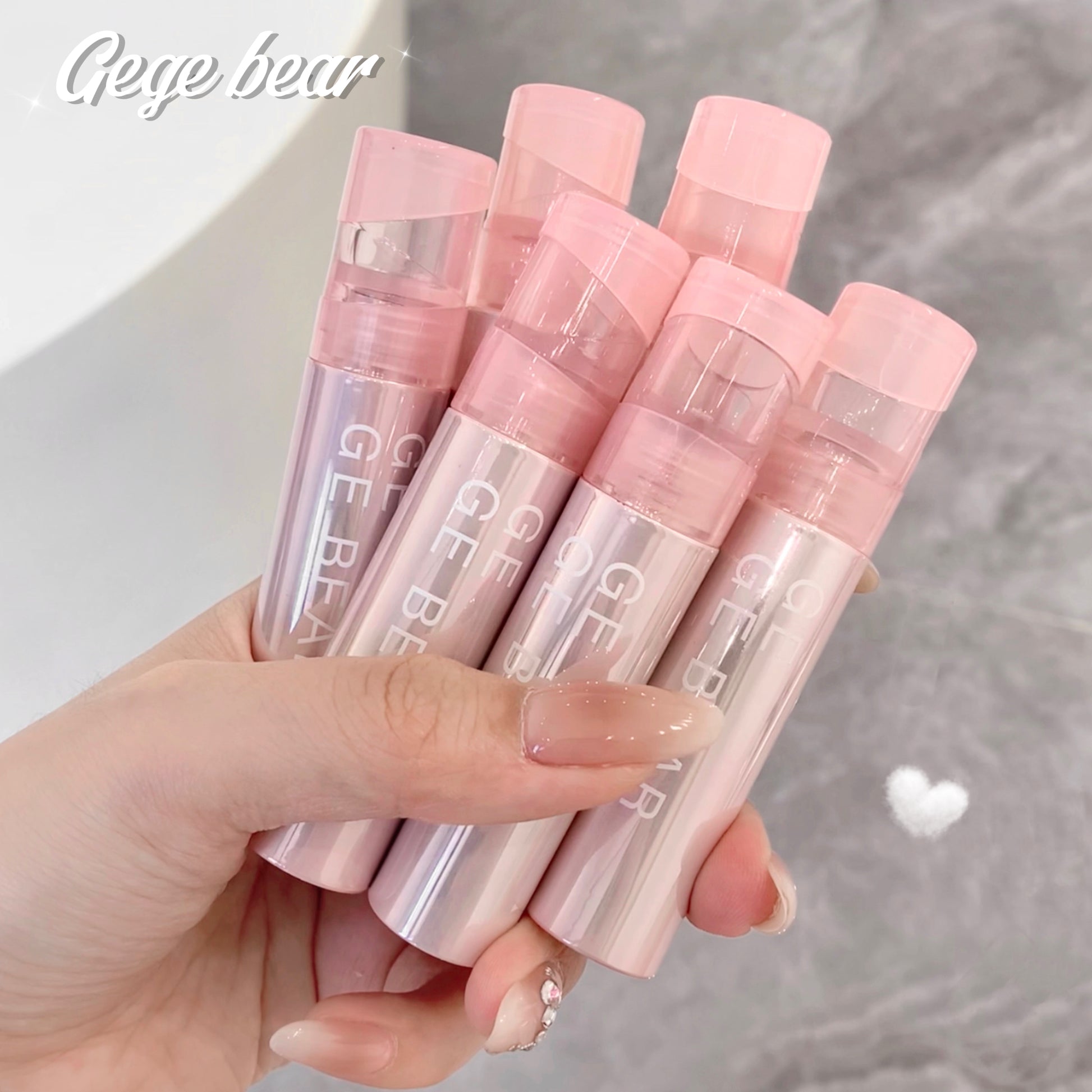 Hand holding pink lip balms with 'Gee Bear' branding against a neutral background