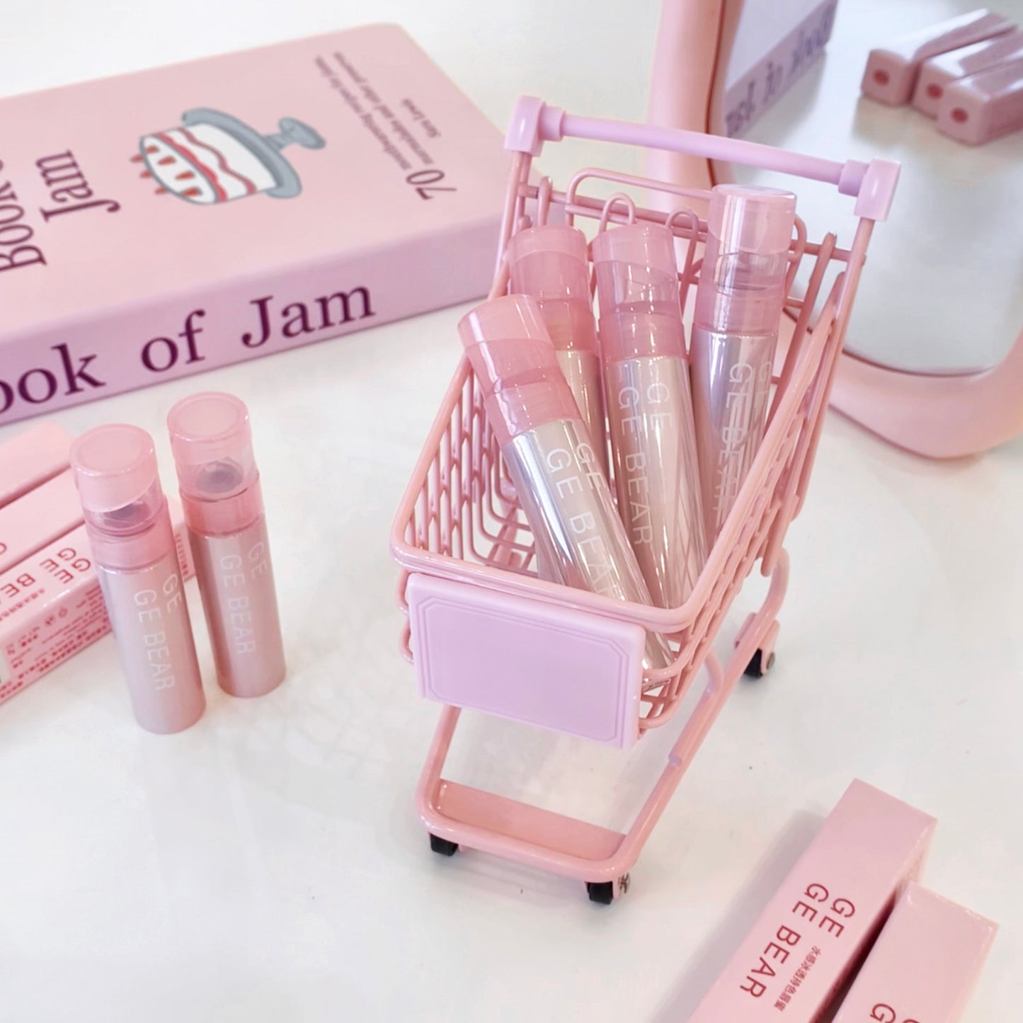 Pink cosmetic products in a mini shopping cart with 'Book of Jam' packaging on a white background