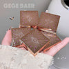 Bronze makeup compact cases with 'G' logo held in a hand, brand 'GEGE BAER' visible.