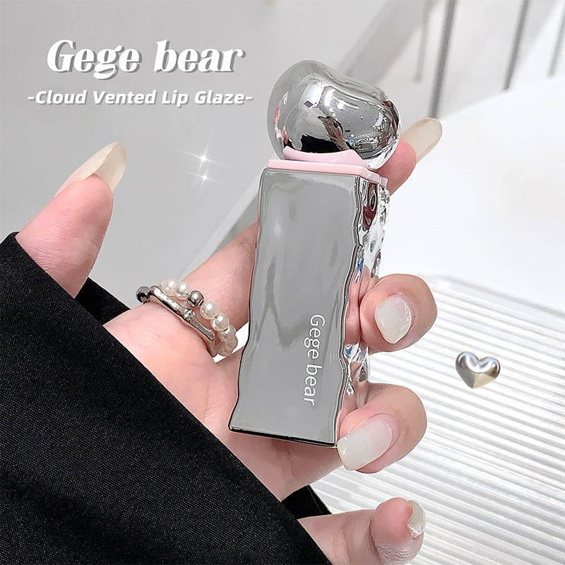 Hand holding a silver 'Gege bear' cloud vented lip glaze against a white background