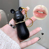 Black bear-shaped keychain held in a hand with a close-up of lips inset.