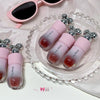 Pink lip glosses with silver accents on a white surface with sunglasses in the background