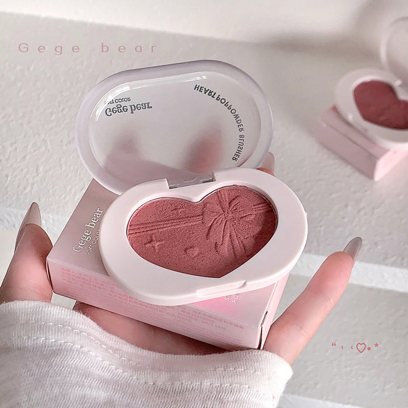 Heart-shaped blush compact with pink blush and 'Gege bear' branding held by a hand.