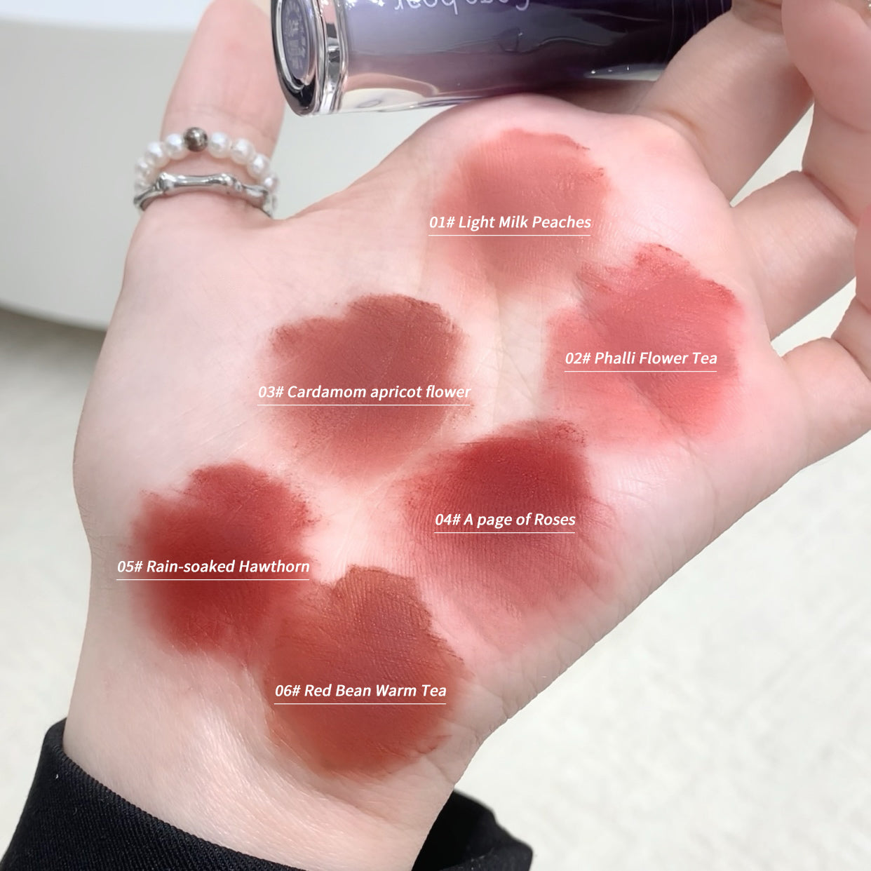 Hand with six different shades of lipstick swatched on a white background