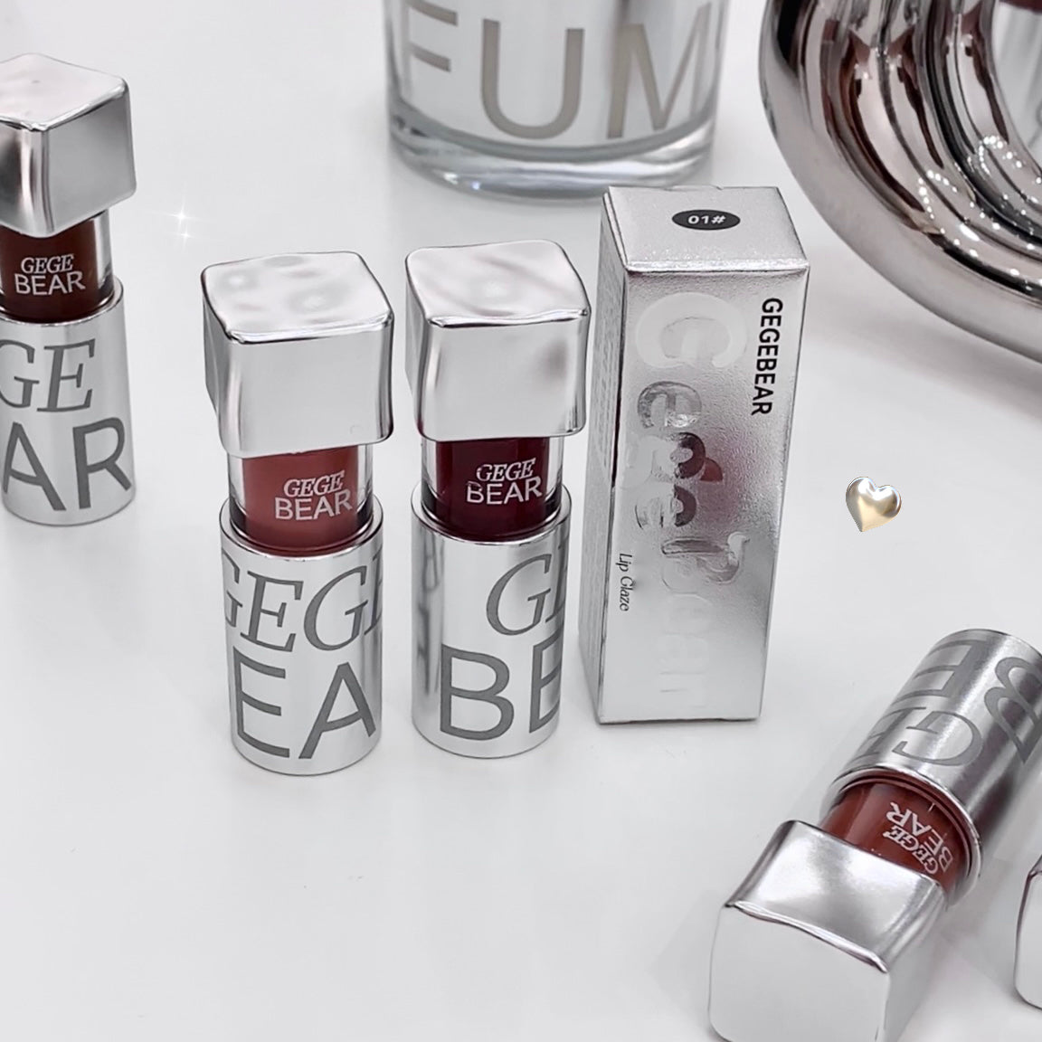 Silver lip gloss bottles with 'GEGEBEAR' branding on a white surface.