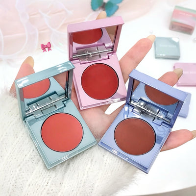 Three compact blushes in different colors held by a hand on a light background