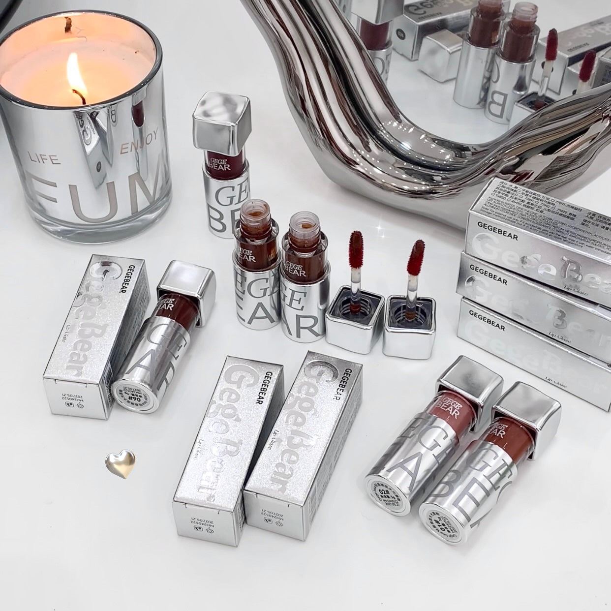 Collection of GEGEREAR lip products including lipsticks and lip glosses on a white surface with a candle and mirror.