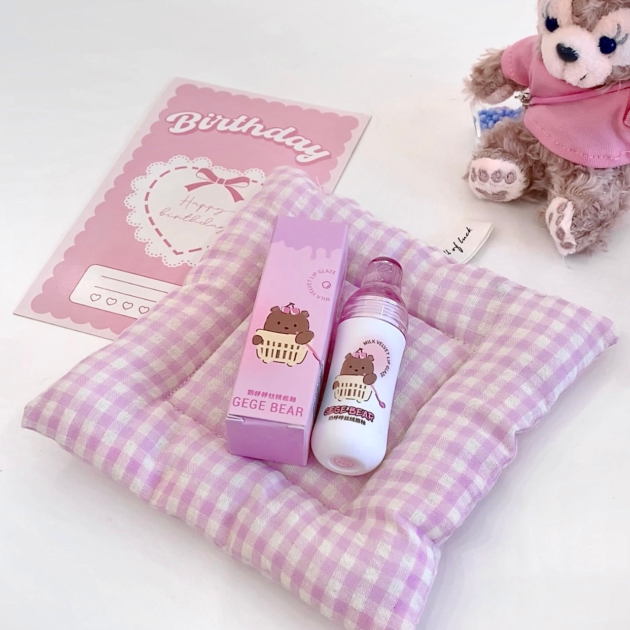 Two bottles with bear designs on a checkered purple and white blanket, next to a pink card and small plush toy.