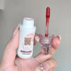 Lip gloss with a bear design on the packaging held by a hand against a neutral background