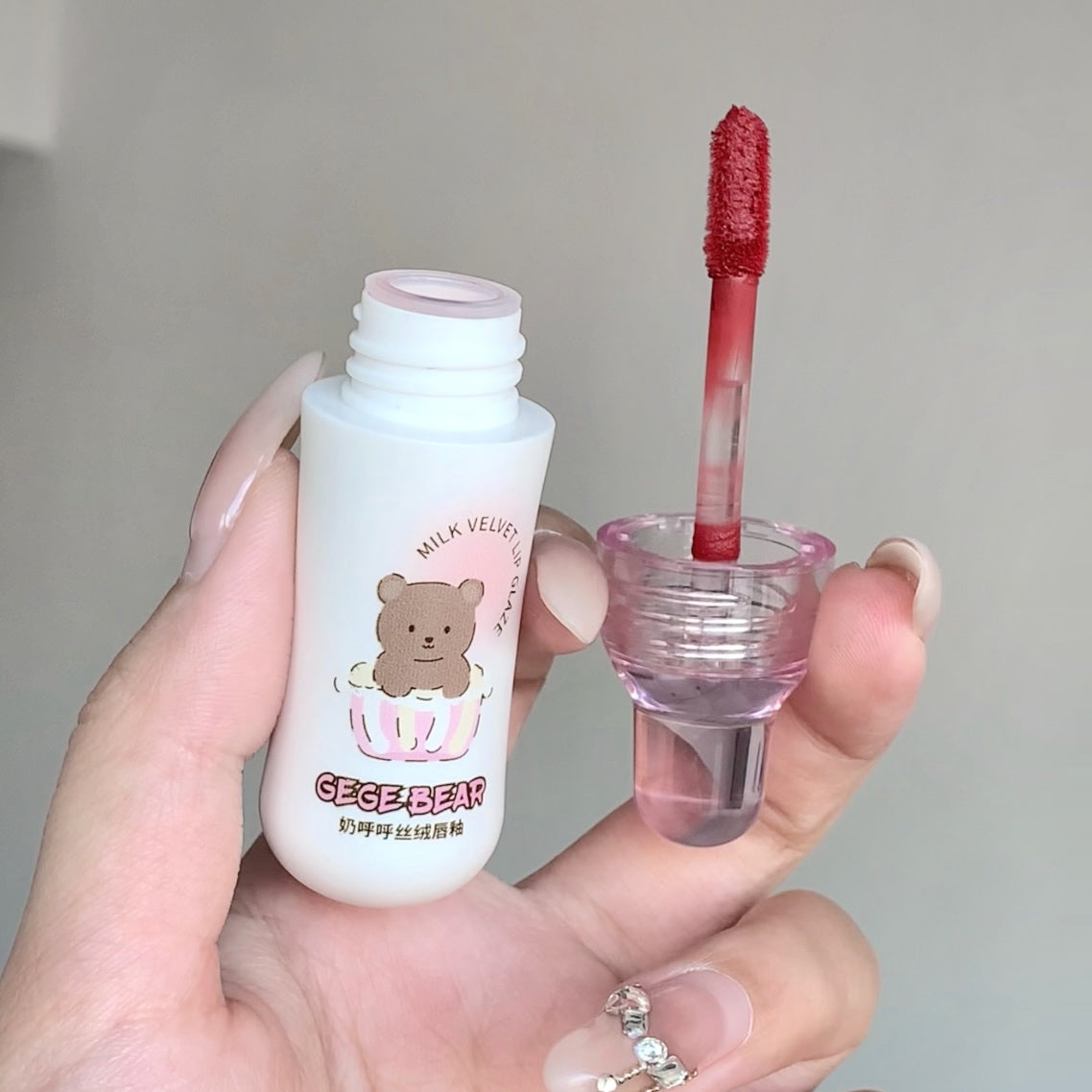 Lip gloss with a bear design on the packaging held by a hand against a neutral background