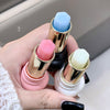 Three lip balms with colorful caps held in a hand against a neutral background