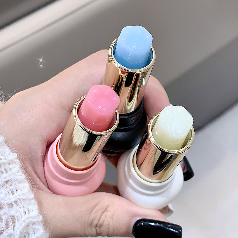 Three lip balms with colorful caps held in a hand against a neutral background