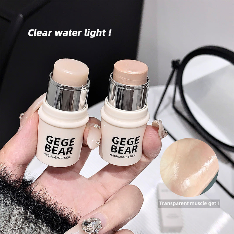 Two GEGE BEAR highlight sticks held in a hand with a mirror and makeup brush in the background.