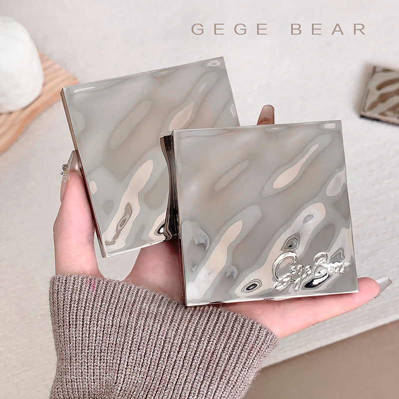 Two metallic compact mirrors held in a hand with 'GEGE BEAR' branding.