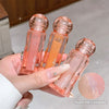 Three transparent lip glosses with pink and orange shades held by a hand.