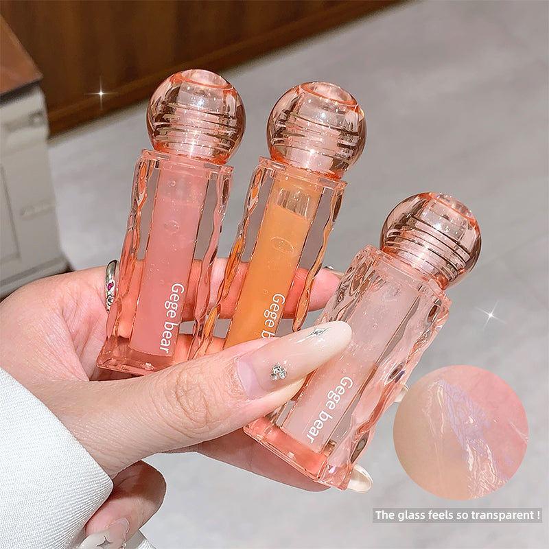 Three transparent lip glosses with pink and orange shades held by a hand.