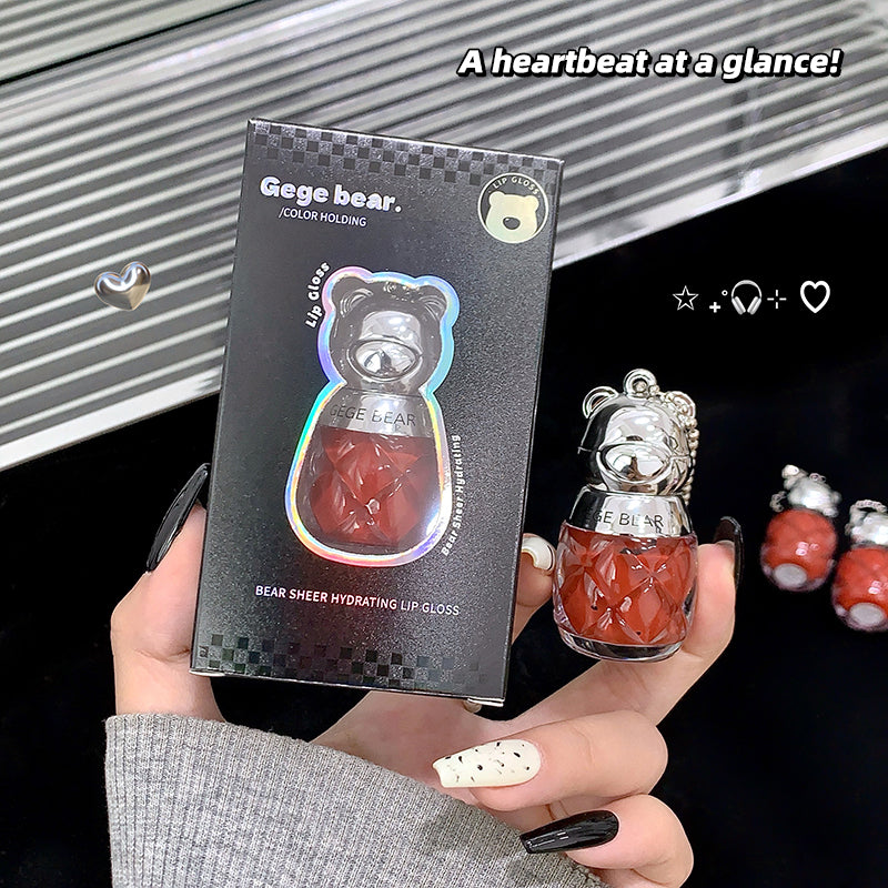 Bear-shaped lip gloss with packaging held by a hand, against a dark background.