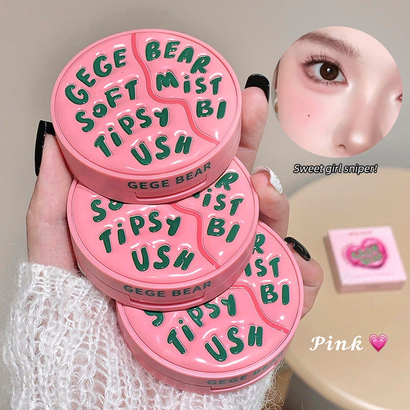 Pink compact mirror with green text held by a hand, close-up of a person's eye, and pink product on a beige surface.