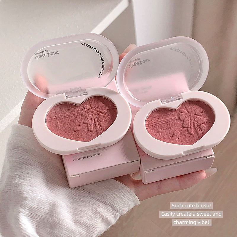 Two heart-shaped blushes in open cases held in a hand with a neutral background.