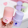 Two lip balm containers, one pink and one purple, held by a hand with a blurred background.
