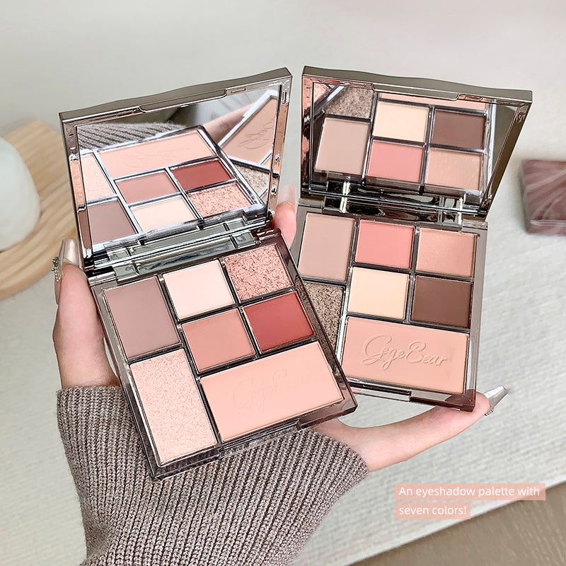 Two open eyeshadow palettes with a variety of colors held by a hand.
