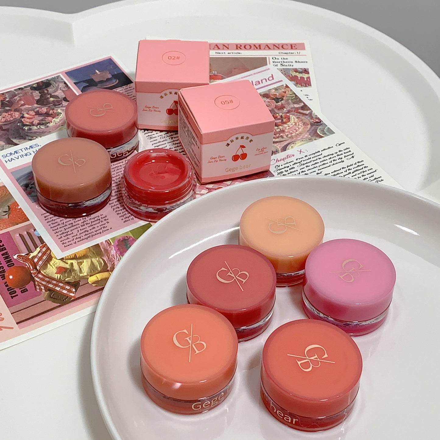 Set of small cosmetic jars with pink lids on a white surface with pink boxes and newspaper in the background.